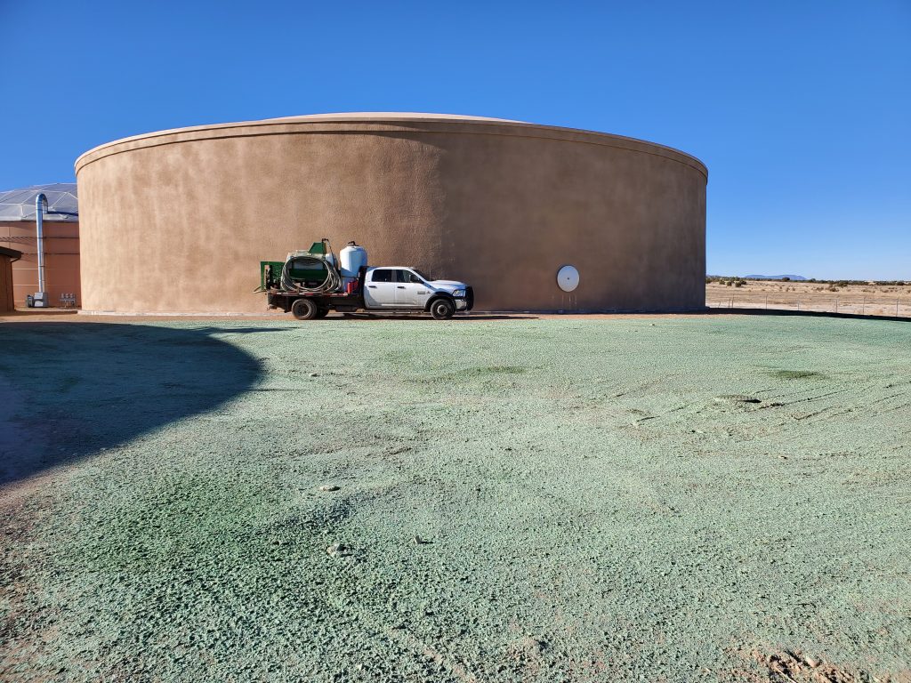 A Foothills Hydroseed truck with hydroturfing equipment in front of a silo with a large area of recent hydroseed in the foreground.