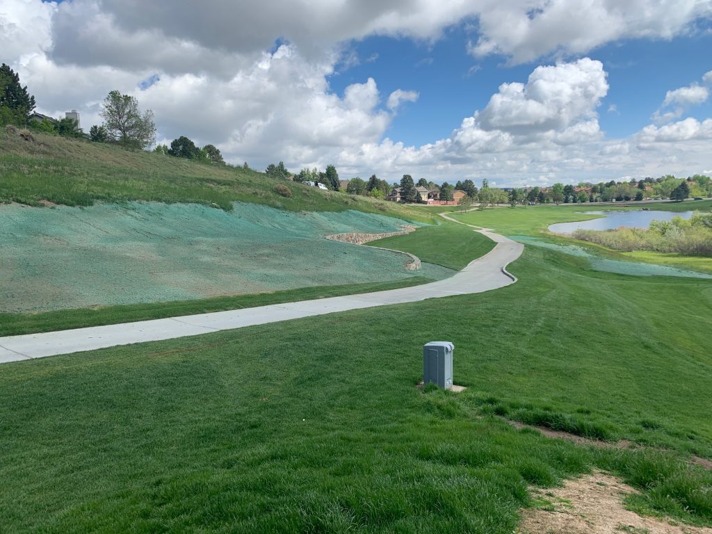 A large area of hill with recent hydroseeding for erosion control next to a long sidewalk in a park.